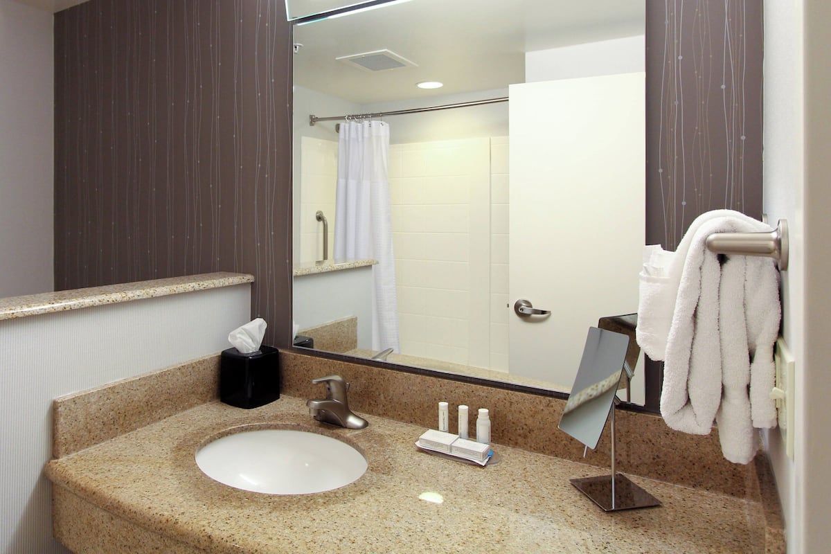 Een badkamer met wastafel, spiegel, handdoekrek en douche.