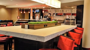 Ein modernes Restaurant mit einer zentralen Kochinsel, roten Stühlen und einem Fernseher im Hintergrund.