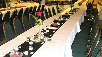 Une salle de banquet avec de longues tables, des chaises et une estrade.