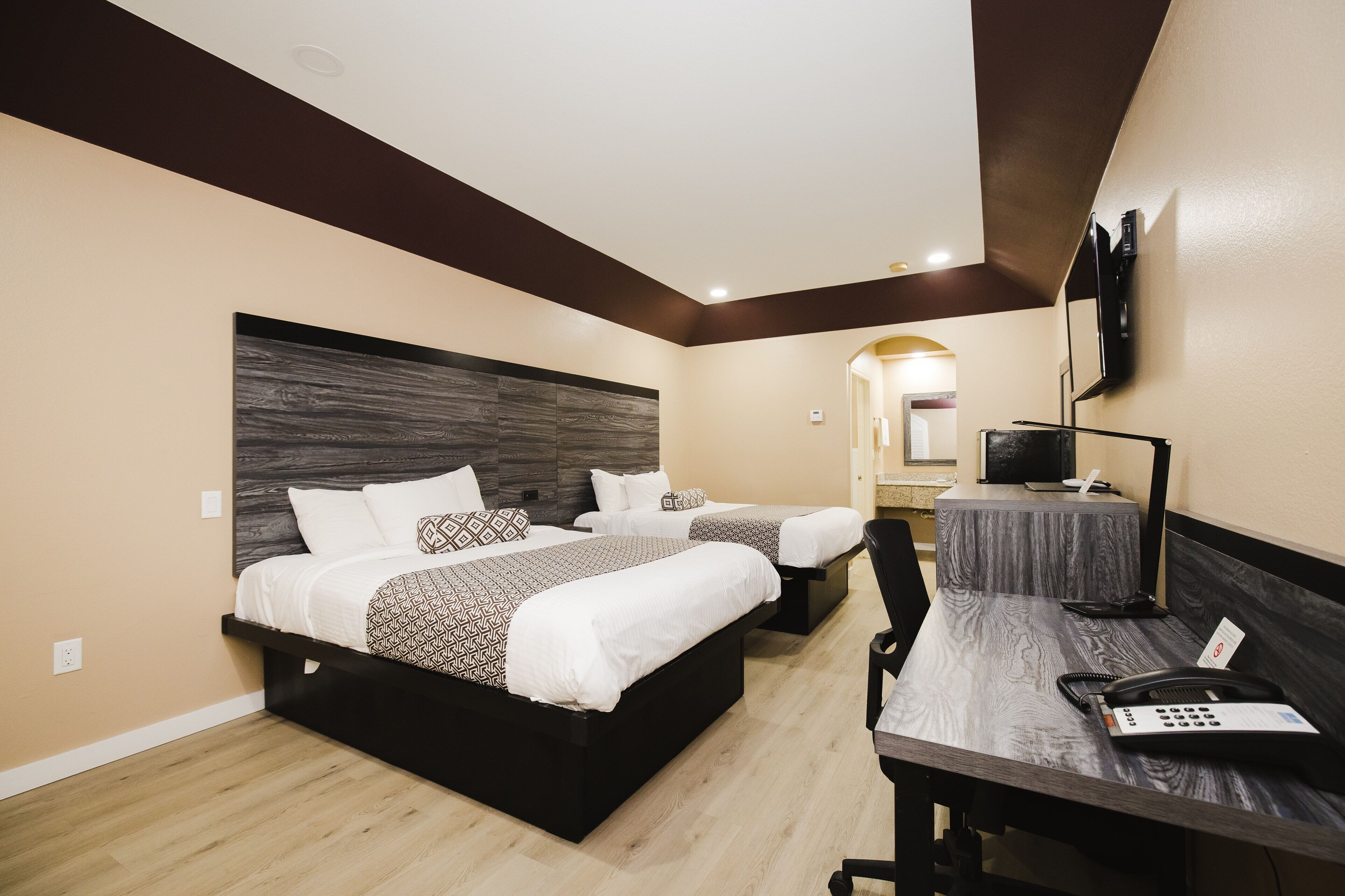 A hotel room with two beds, a desk with a telephone, and a television on the wall.