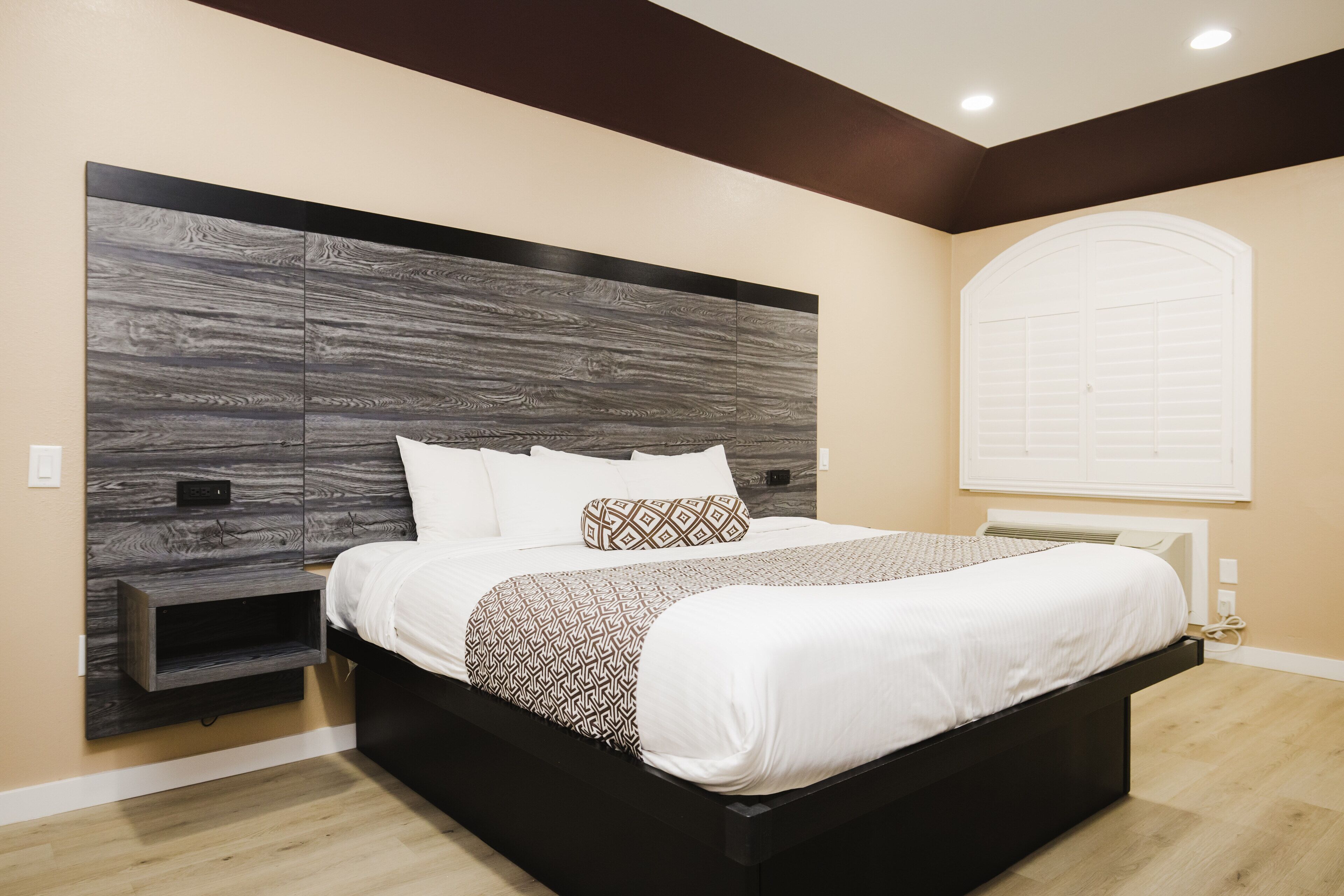 A modern bedroom with a large bed, built-in headboard, and a window with blinds.