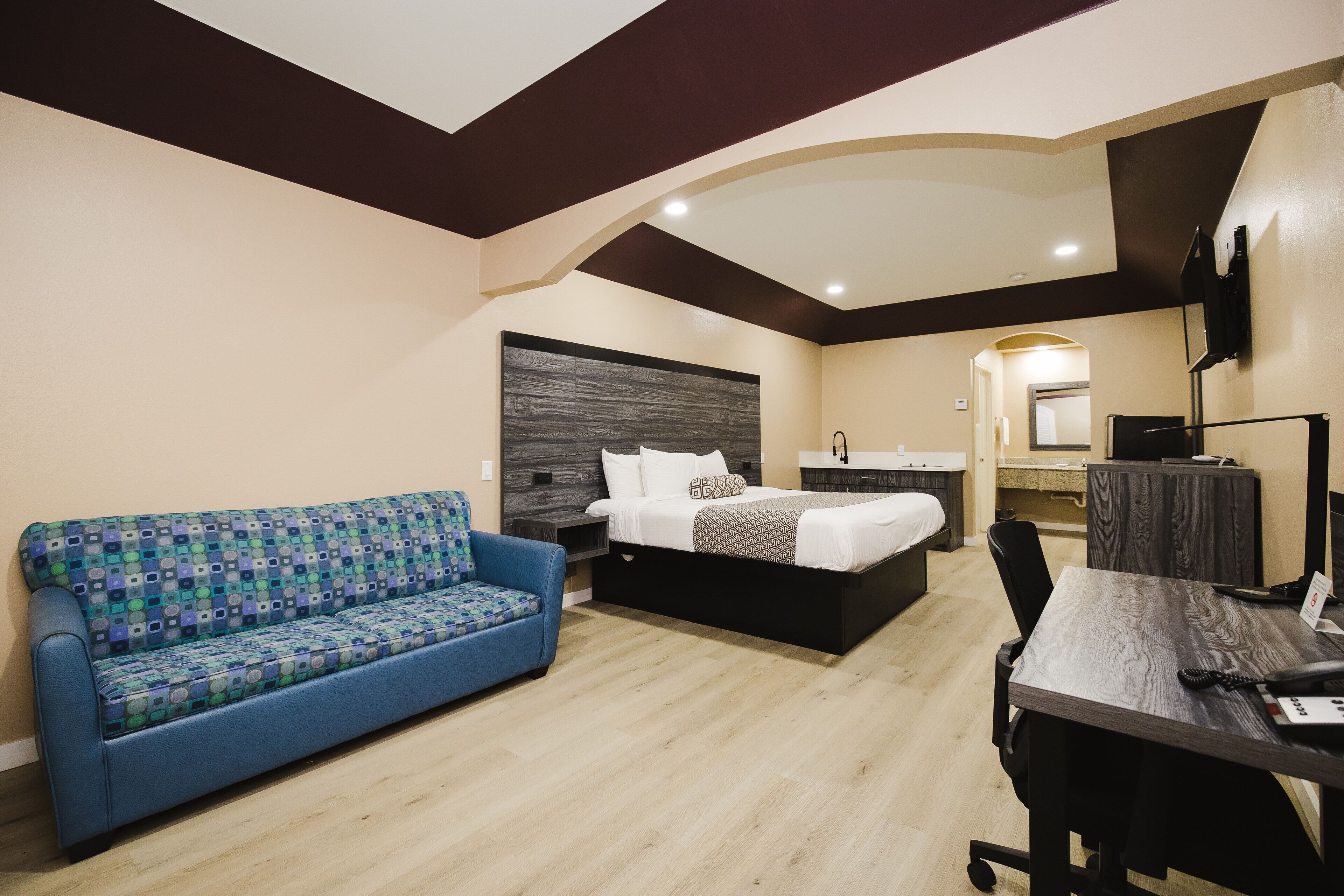 A modern hotel room with a sofa, a bed, a desk, and a mirror.