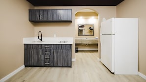 A modern kitchen with dark wood cabinets, a white refrigerator, and a beige countertop. - Sapphire Inn & Suites (Channelview)