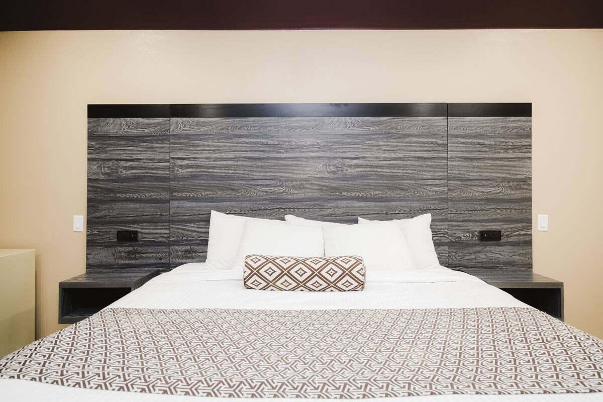 Ein modernes Hotelzimmer mit einem großen Bett, einer gestreiften Tagesdecke und einem Kopfteil mit Holzoptik.