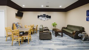 A hotel lobby with a dining area, sofas, a television, and a cityscape artwork on the wall. - Sapphire Inn & Suites (Channelview)