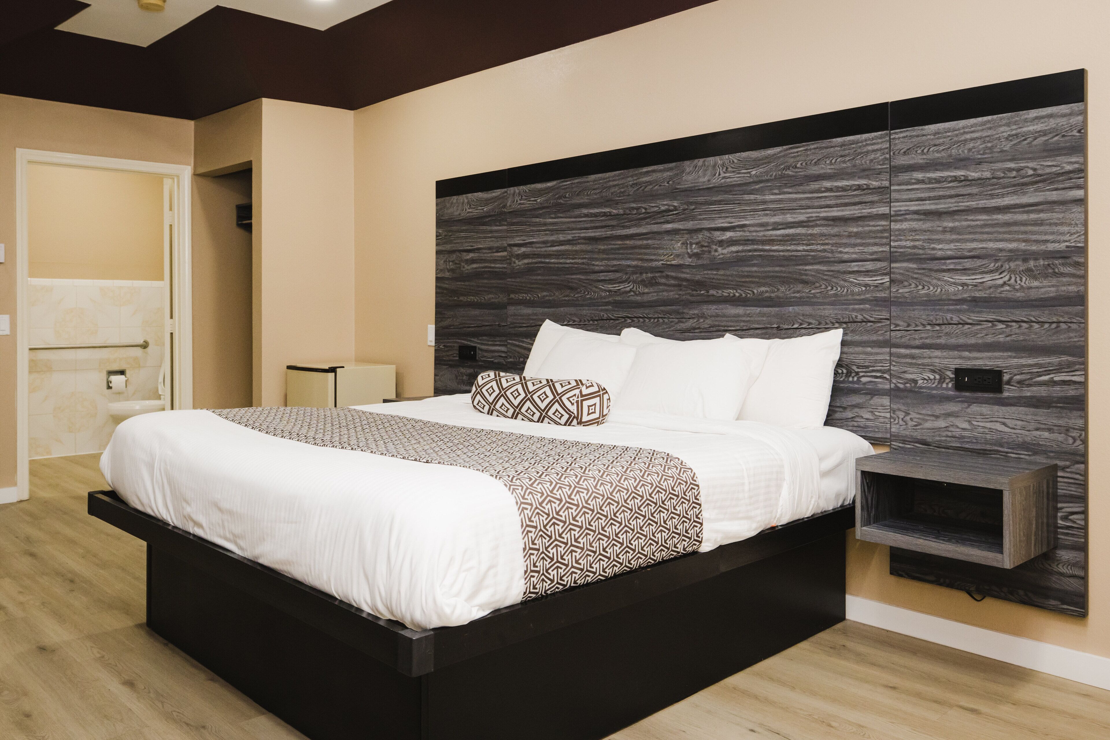 A modern bedroom with a large bed, a wooden headboard, and a bedside table.