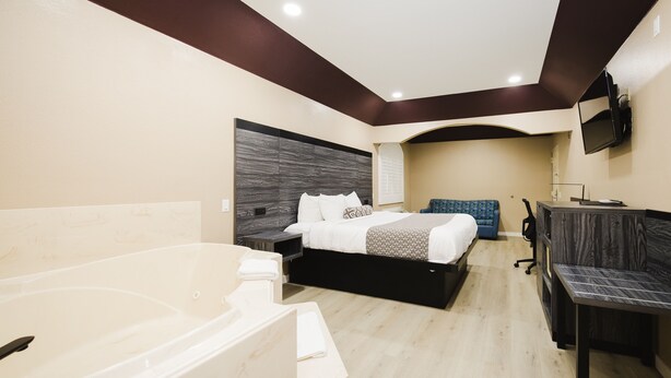 A modern hotel room with a large bathtub, a bed with a headboard, a desk, and a flat-screen TV mounted on the wall. - Sapphire Inn & Suites (Channelview)