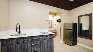 A modern kitchen with a double sink, dark wood cabinetry, a stainless steel refrigerator, and a large mirror. - Sapphire Inn & Suites (Channelview)