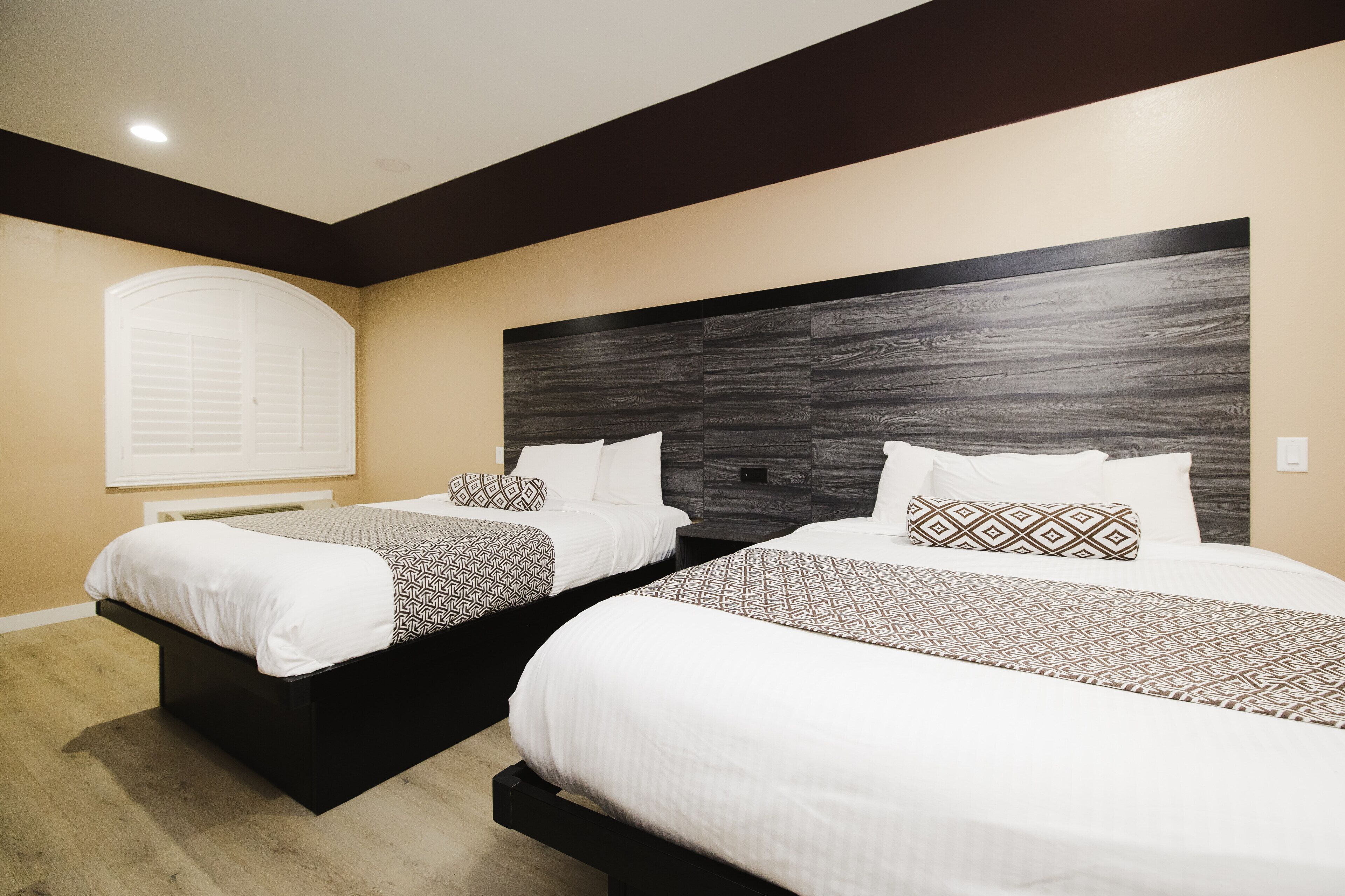 A hotel room with two beds, a dark wood headboard, and a window with blinds.