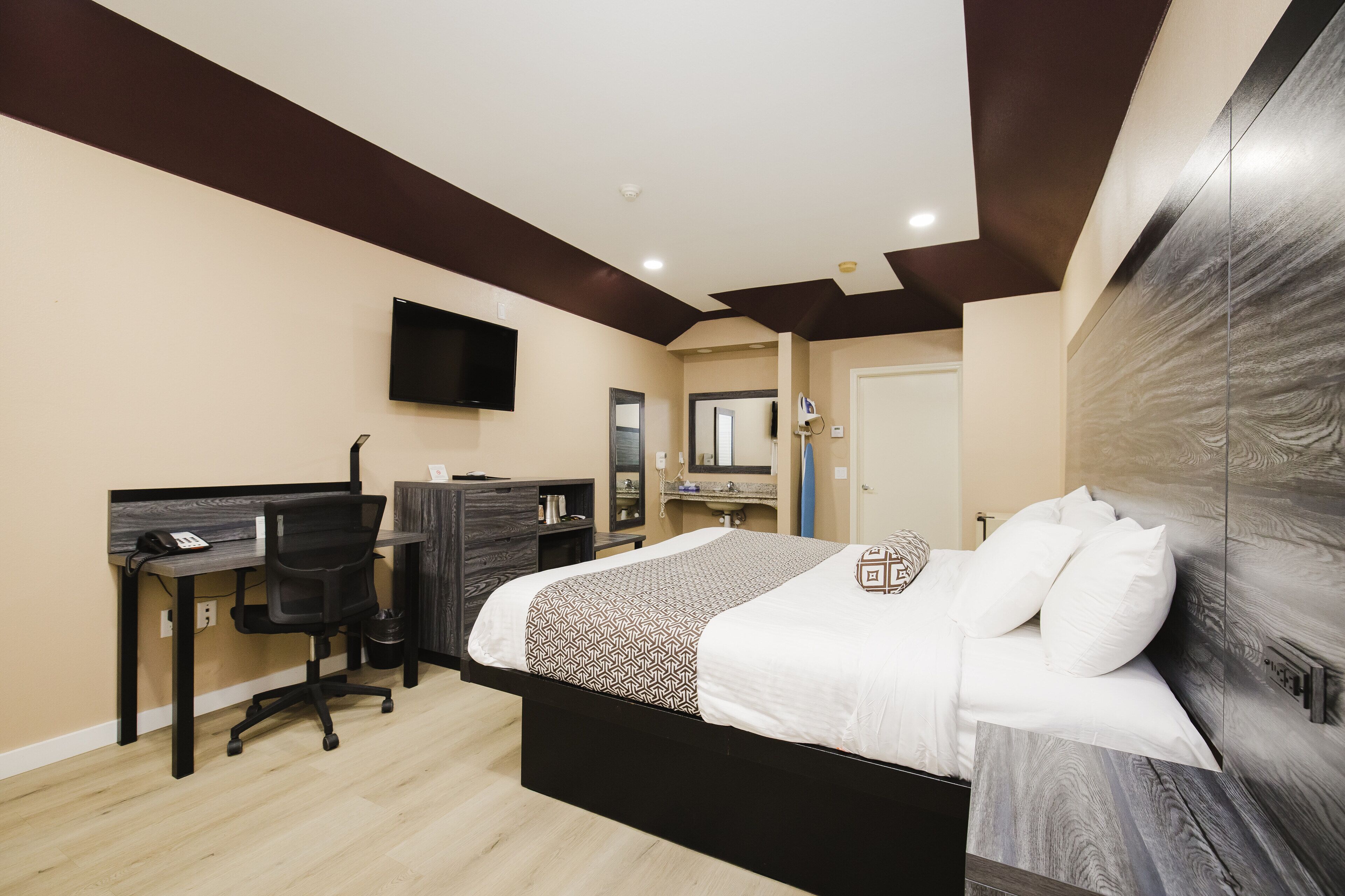 A modern bedroom with a large bed, a desk, and a TV.