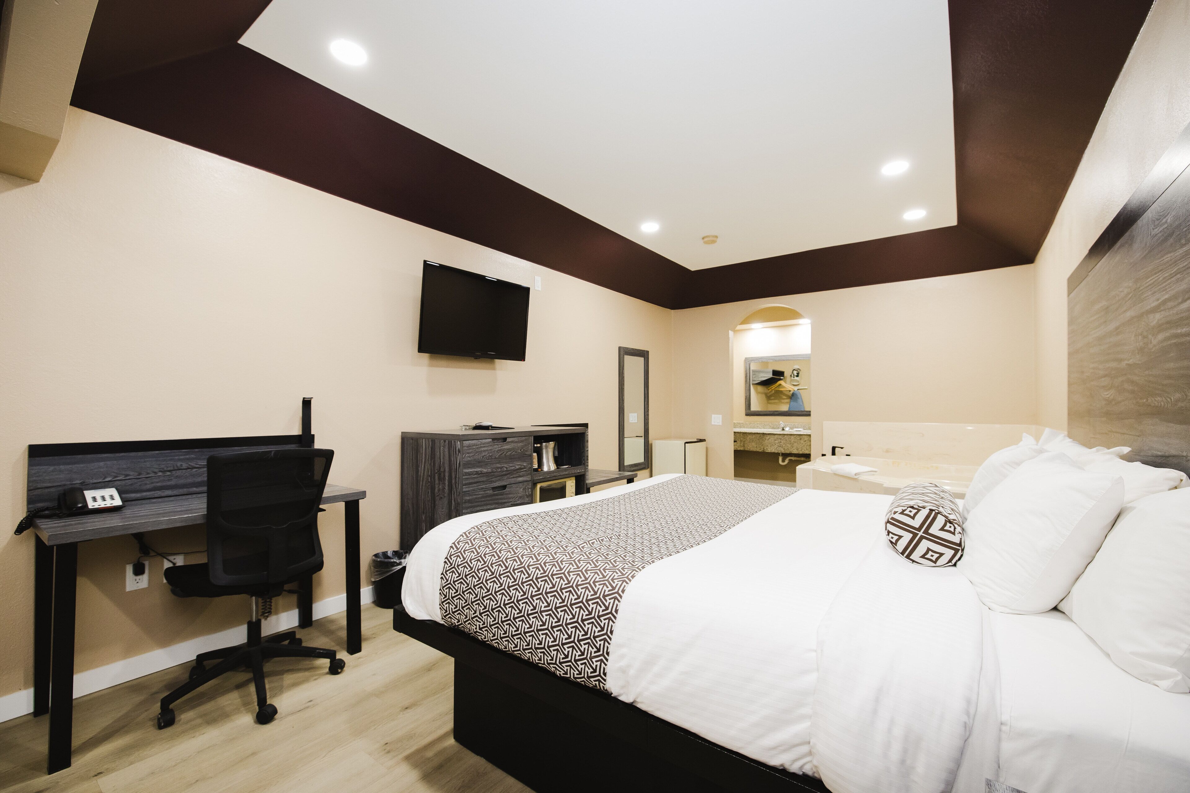 Une chambre d’hôtel moderne équipée d’un lit, d’un bureau, d’une chaise et d’un téléviseur fixé au mur.