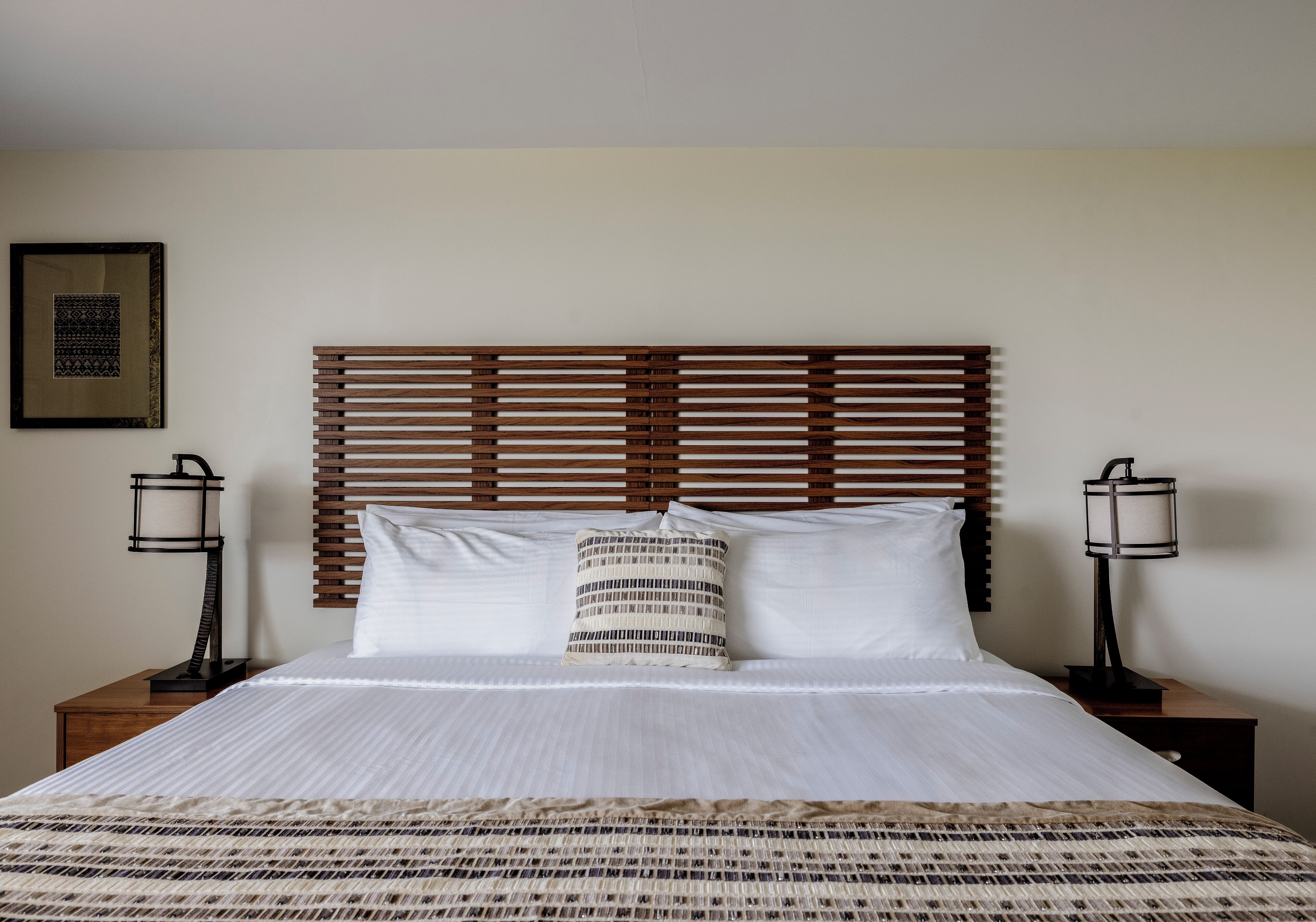 Una cama bien hecha con una colcha estampada, cabecera de madera y dos lámparas de noche.