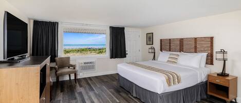 Une chambre d’hôtel comprenant un lit, un bureau, une chaise, une télévision, une fenêtre donnant sur la plage et une table de chevet avec une lampe.