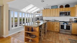 A kitchen with wooden cabinets, a stainless steel microwave, and a large island with blue vases. - Dune Crest Hotel (North Truro)