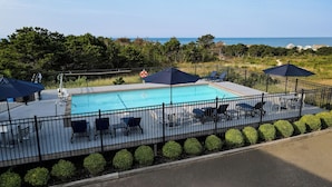 A pool area with a view of the ocean, surrounded by a fence and chairs. - Dune Crest Hotel (North Truro)