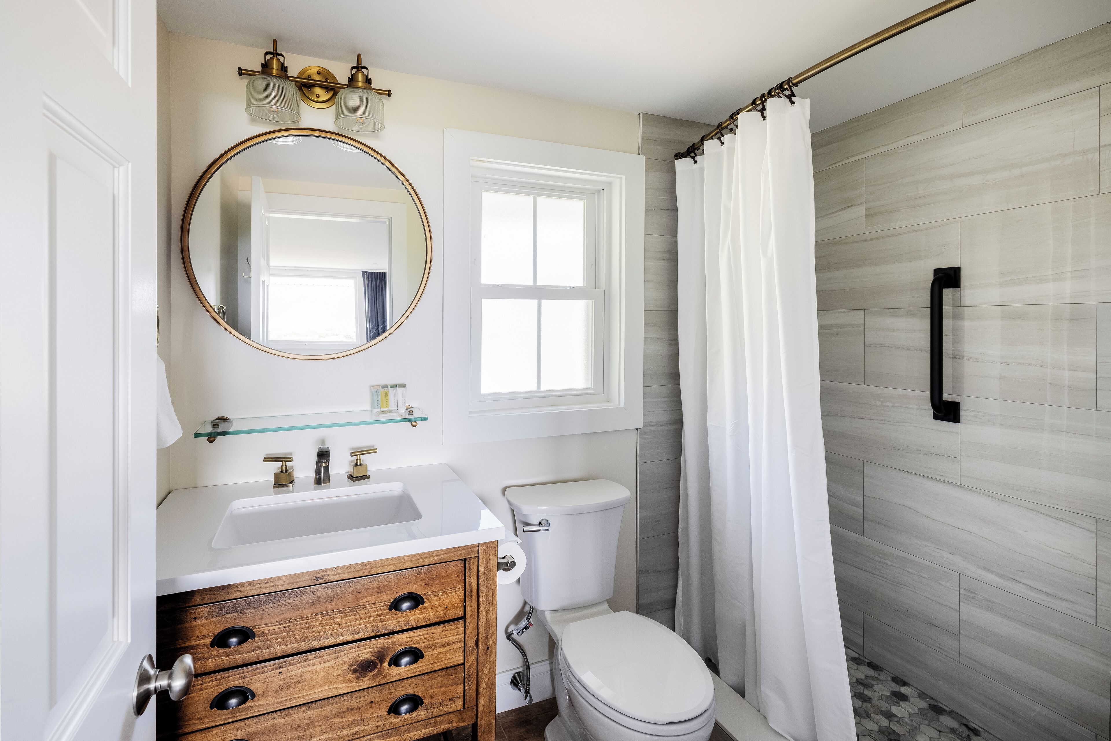 A bathroom with a white sink, wooden vanity, a round mirror, a toilet, and a shower curtain.