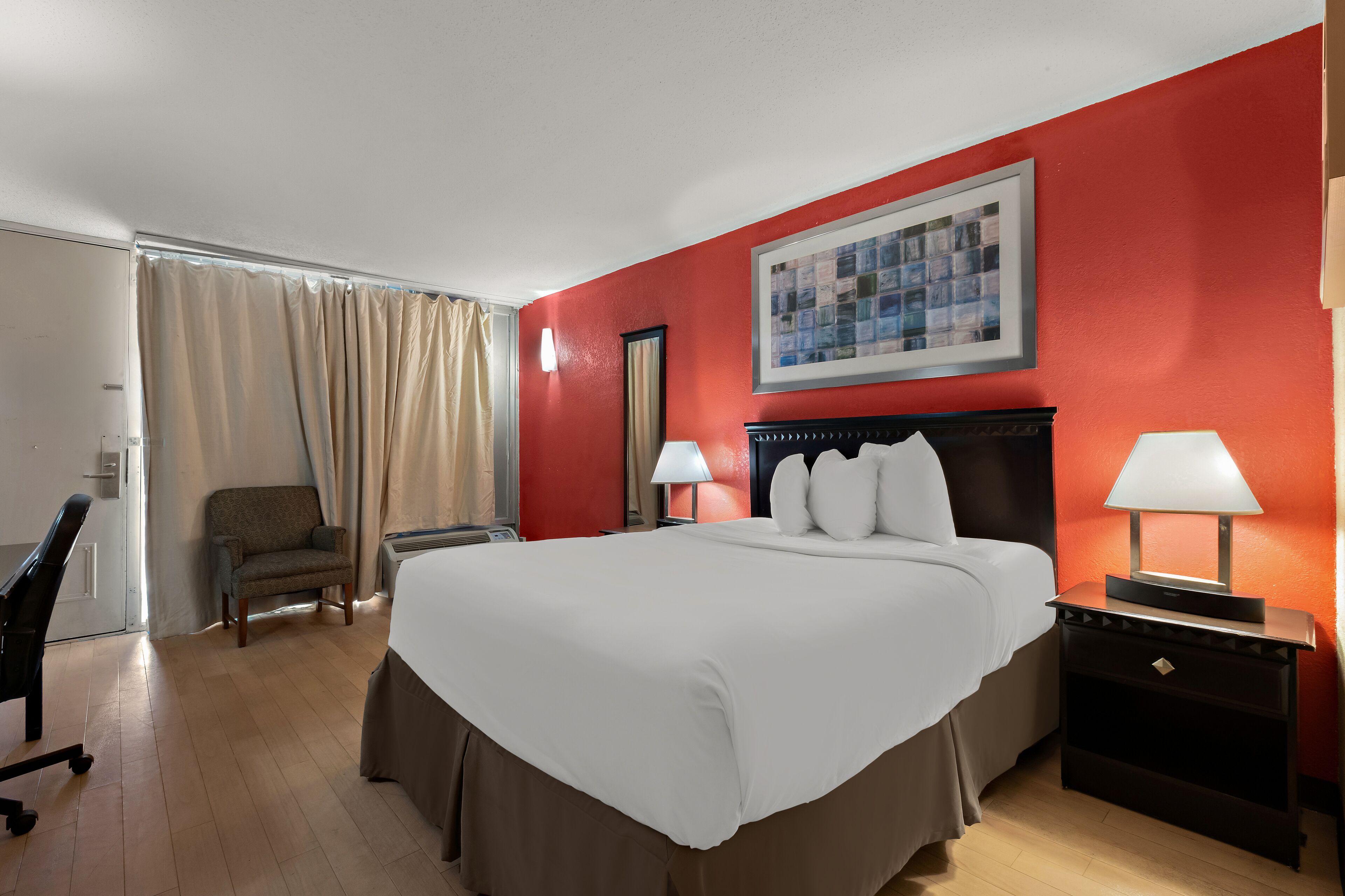 A hotel room with a large bed, two bedside lamps, a chair, a desk, and a window with curtains.