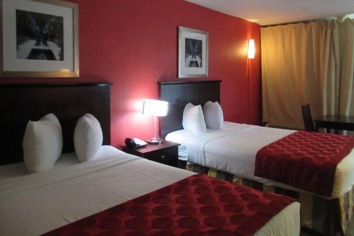 A hotel room with two beds, a nightstand, a lamp, and a chair.