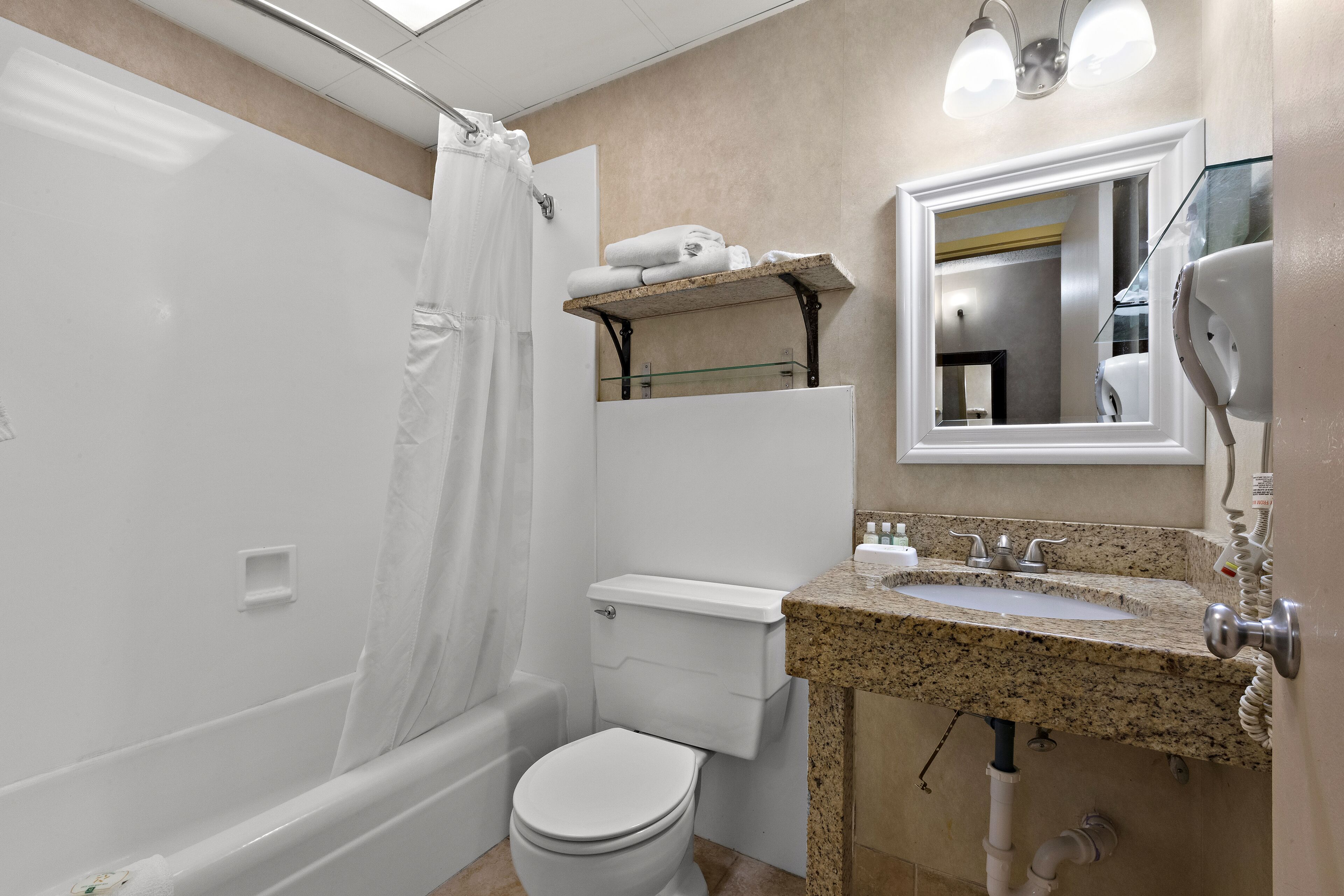 A bathroom with a shower, toilet, sink, and a mirror.