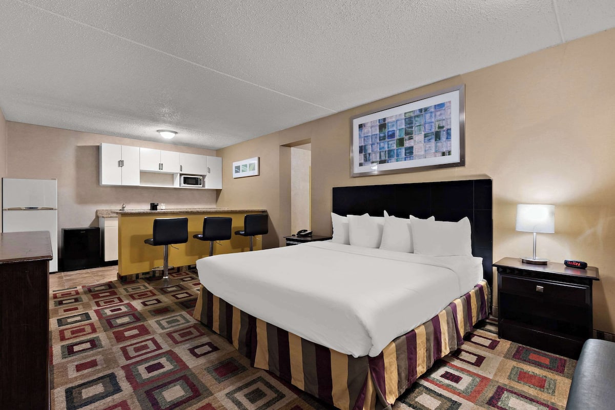 Quarto de hotel com cama, escrivaninha, cadeira, micro-ondas e pequena cozinha.