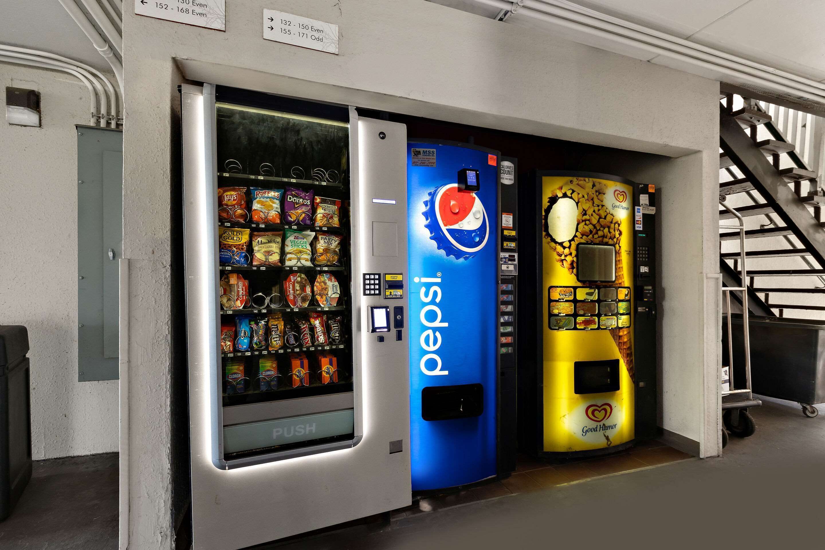 Three vending machines, one for Pepsi, one for Doritos, and one for Great Value snacks, in a hallway.