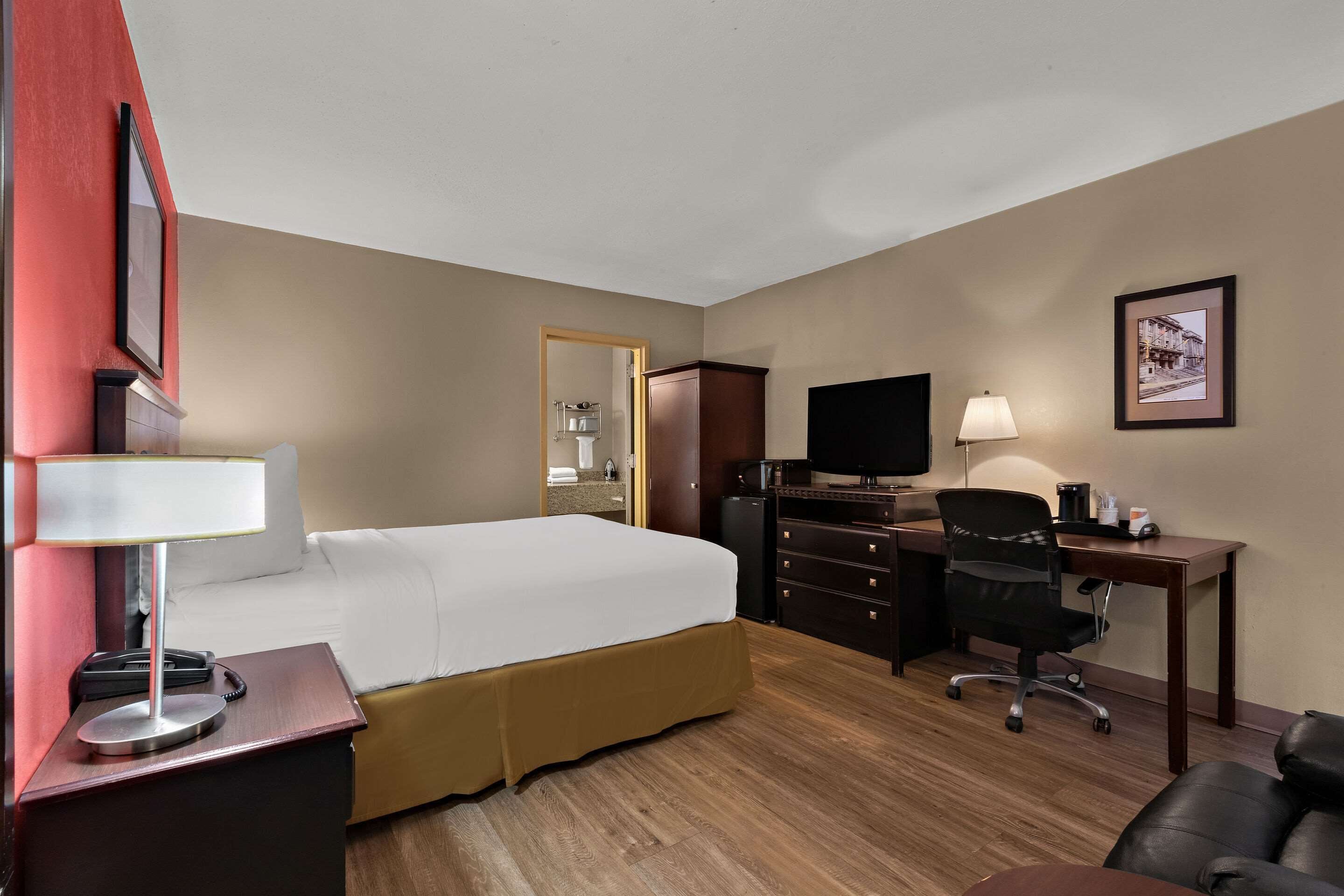 A hotel room with a bed, a desk with a chair, a television, and a desk lamp.