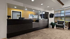 Zona de recepción con diseño moderno, que incluye un mostrador de recepción, un cartel y un área de descanso con una silla.