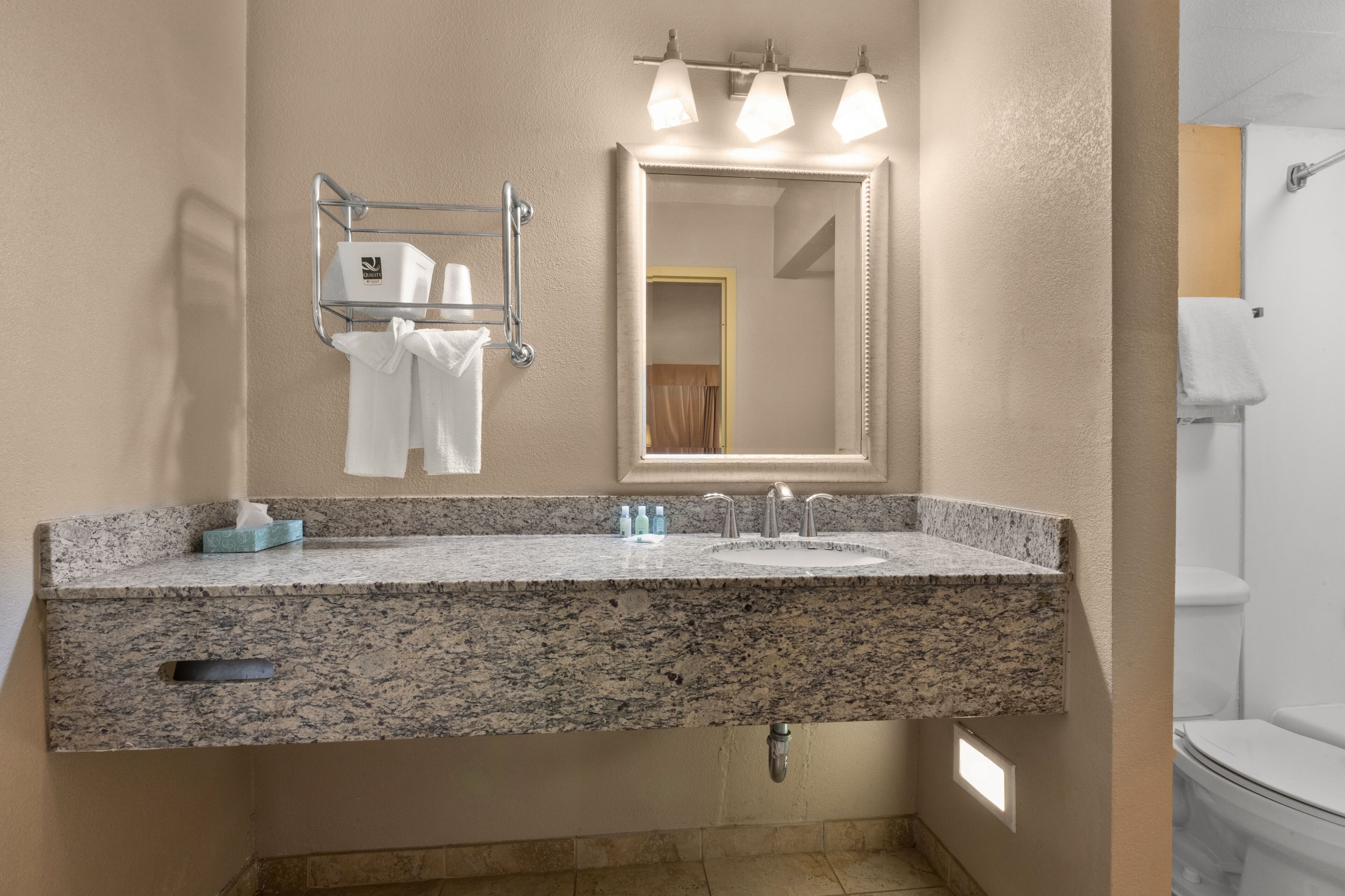 Un baño con lavamanos de encimera de granito, un espejo y un perchero para toallas.