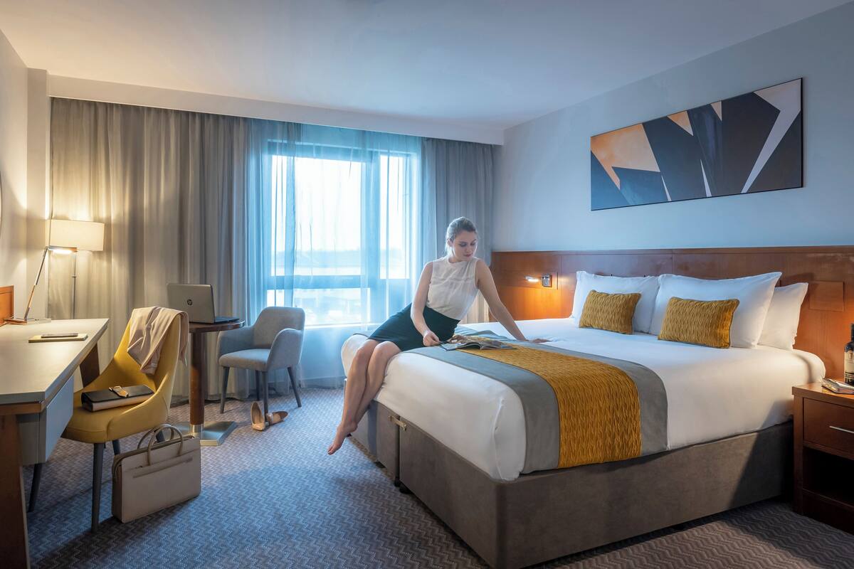 Ein Hotelzimmer mit einem Bett, einem Schreibtisch, einem Stuhl, einer Lampe und einem fenster mit Vorhängen.