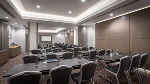A conference room with multiple tables and chairs, equipped with water bottles and glasses, and a large screen at the front. - Maldron Hotel Sandy Road Galway (Galway)