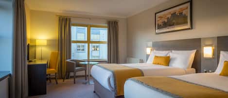 A hotel room with two beds, a desk, a chair, a window with curtains, and a painting on the wall.