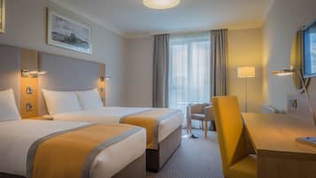 A hotel room with two beds, a desk, a chair, a small table, and a window with curtains.