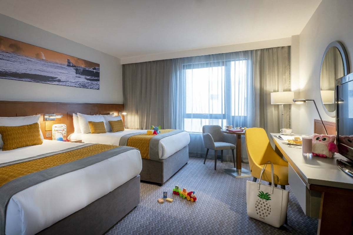 Une chambre d’hôtel avec deux lits, un bureau, une chaise, une télévision et un tableau au mur.