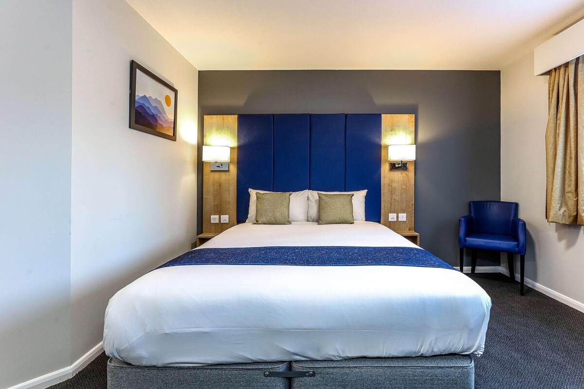 Habitación de hotel con una cama grande, dos lámparas fijadas a la pared, una silla y un cuadro.