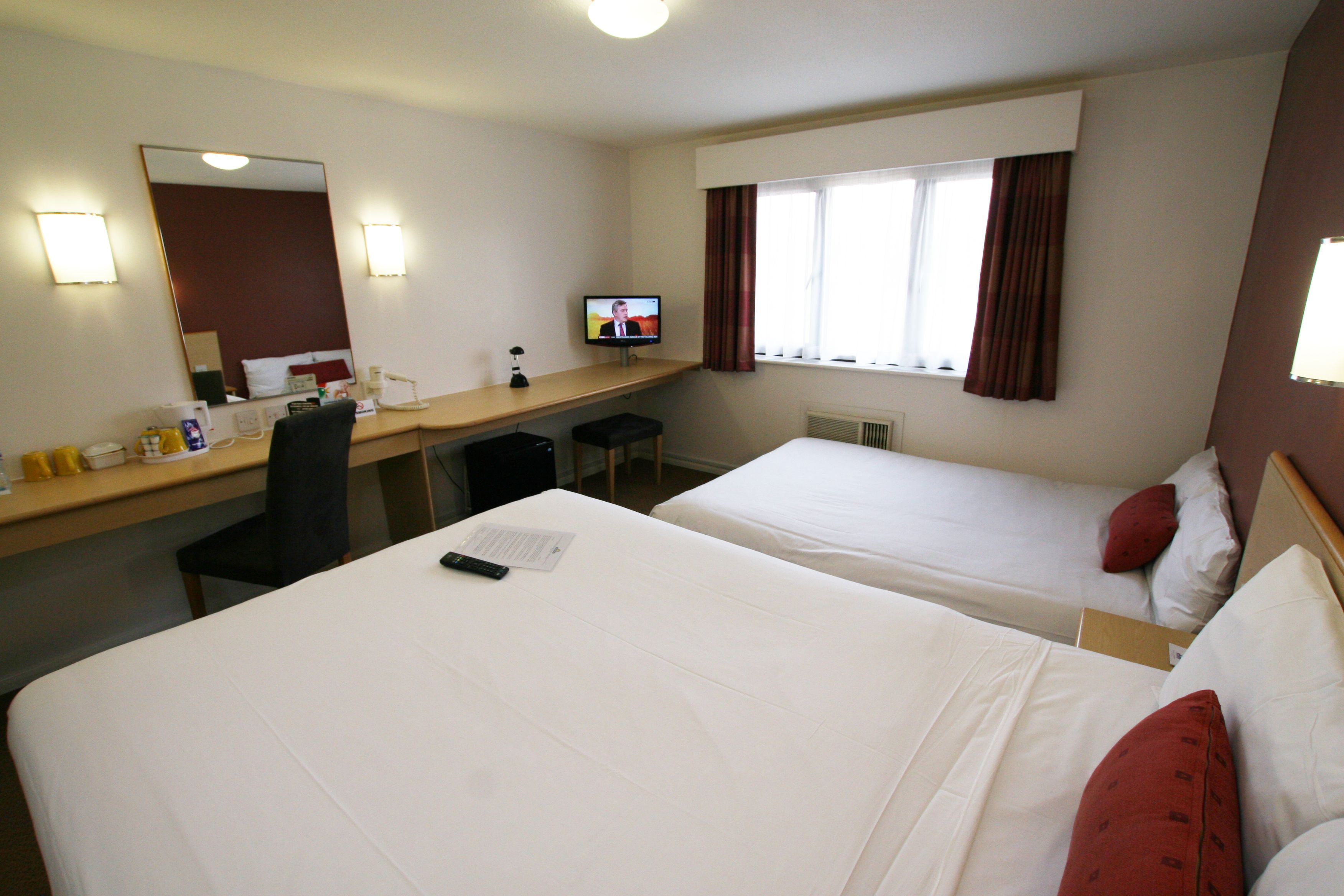 Habitación de hotel con dos camas, un escritorio con computadora, una silla y un televisor.