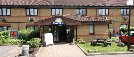 Un bâtiment de la chaîne Days Inn, avec une enseigne, un panneau indiquant l’accessibilité aux personnes à mobilité réduite, une poubelle et une table de pique-nique.