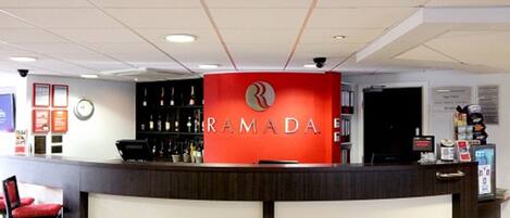 A reception area with a red counter, a clock, and a bar with various bottles.