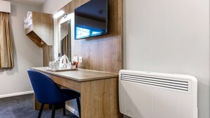 A hotel room with a wooden desk, a blue chair, a flat-screen TV mounted on the wall, and a white radiator. - Days Inn by Wyndham London Stansted Airport (Bishop's Stortford)