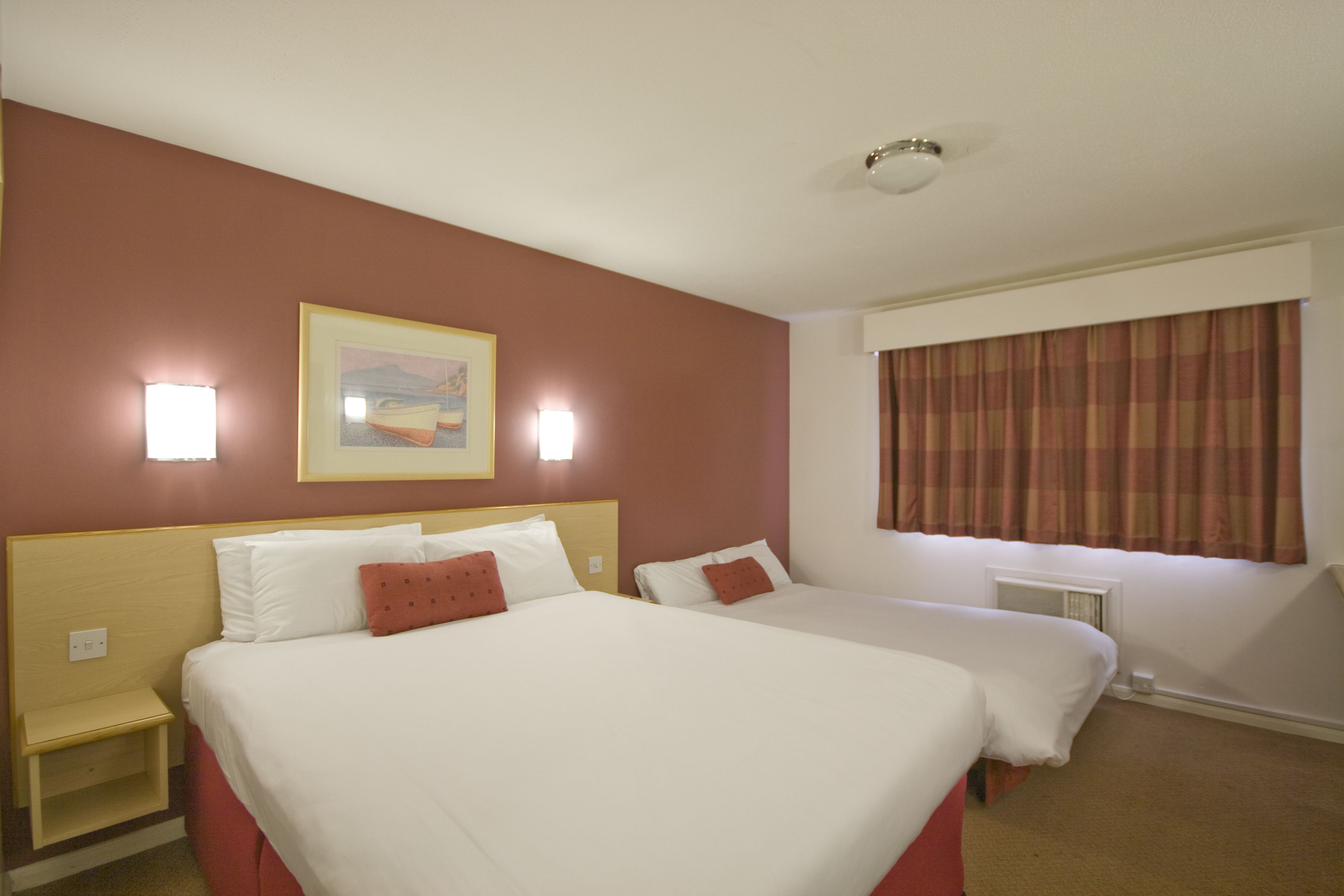 Quarto de hotel com duas camas, um quadro na parede e uma janela com cortinas.