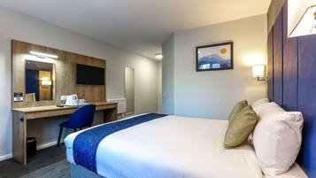A hotel room with a bed, a desk, a chair, a desk lamp, a trash bin, and a wall-mounted TV.