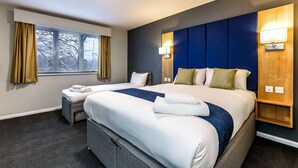A hotel room with two beds, a large window with curtains, a wall-mounted lamp, and a small wooden shelf. - Days Inn by Wyndham London Stansted Airport (Bishop's Stortford)