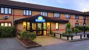 A Days Inn hotel with a brick facade, a signboard, and a well-lit entrance. - Days Inn by Wyndham London Stansted Airport (Bishop's Stortford)
