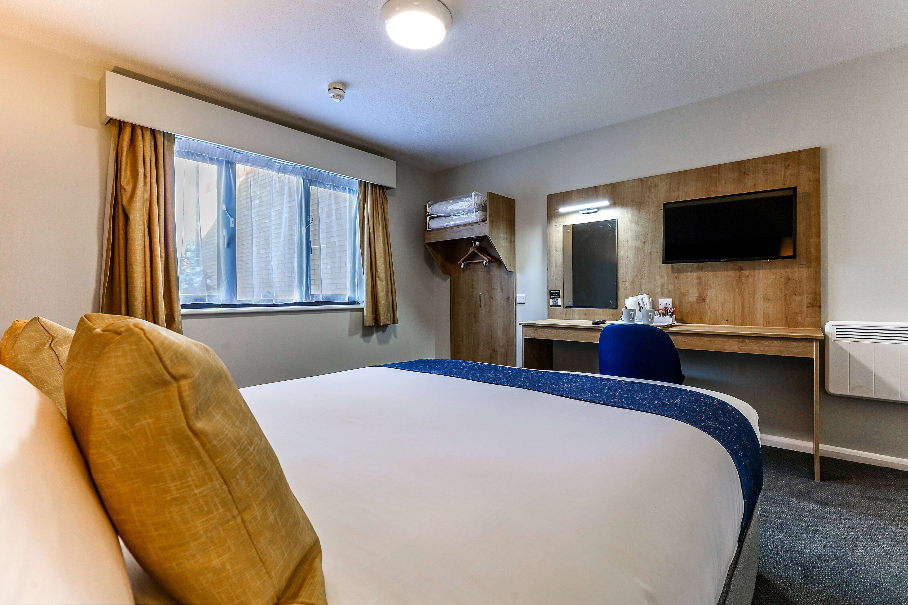 A hotel room with a large bed, a desk, a chair, a TV, and a window with curtains.