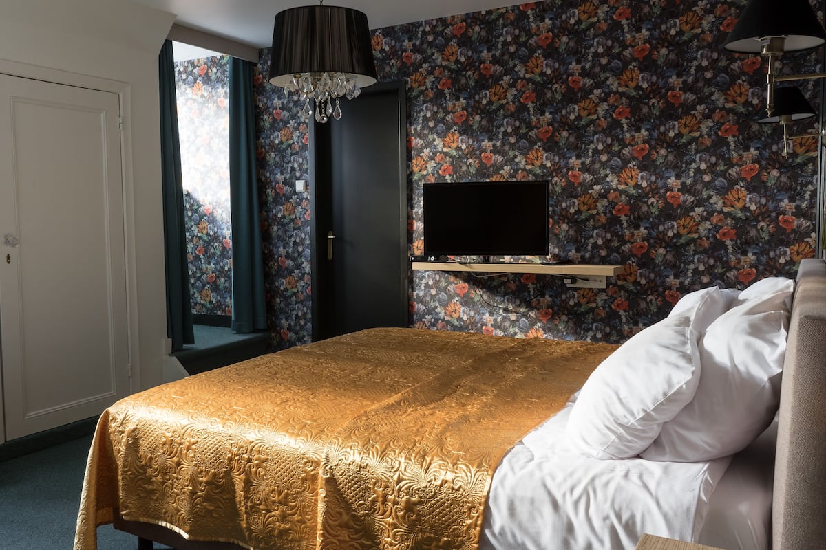 A bedroom with a bed, a TV mounted on the wall, and a floral wallpaper.