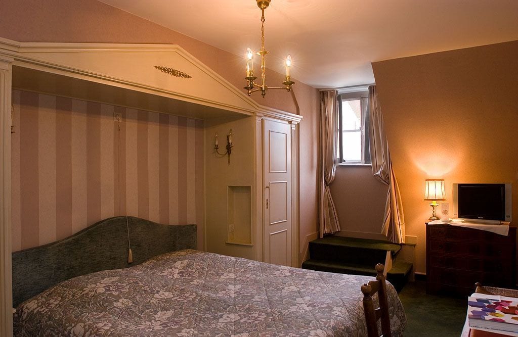 Een slaapkamer met een groot bed, een televisie, een bureau en een raam met gordijnen.