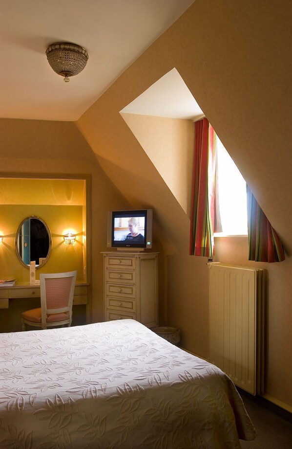 A bedroom with a bed, a television, a chair, a desk, and a mirror. - Duc de Bourgogne (Bruges)