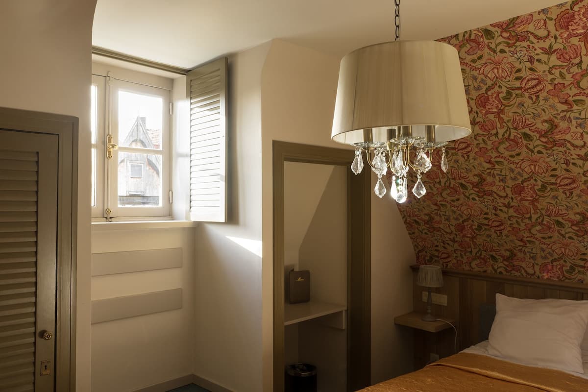 A bedroom with a window, a chandelier, a bed, and a nightstand.