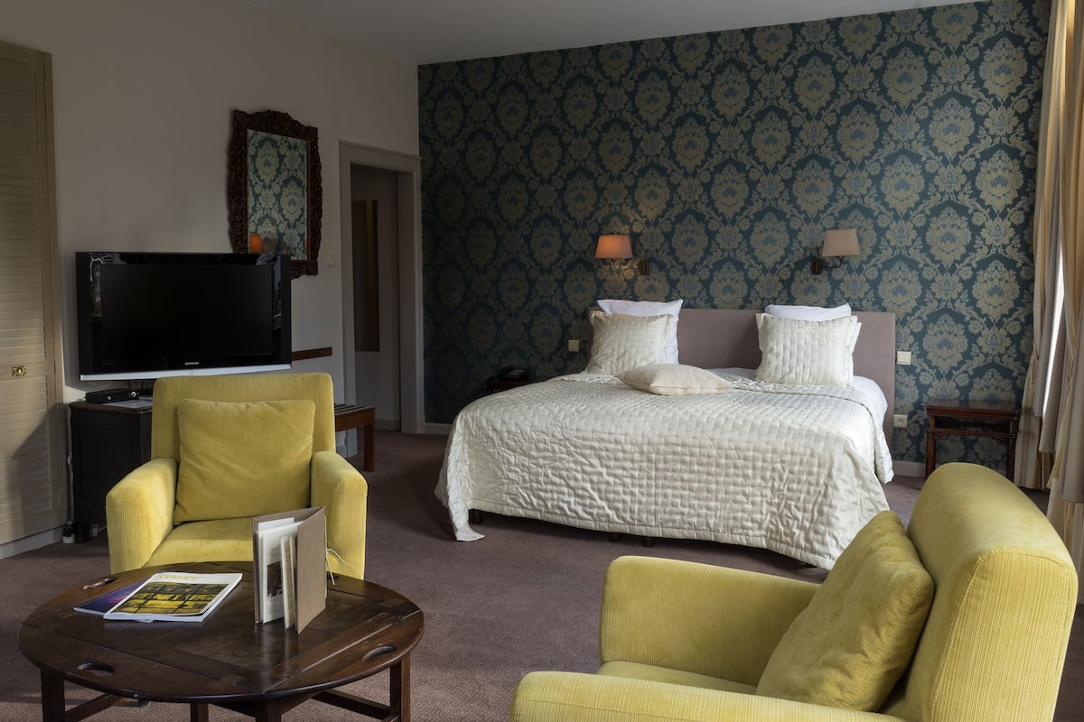 A hotel room with a large bed, two bedside lamps, a television, and two yellow armchairs.