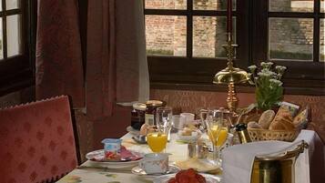 Una mesa de desayuno preparada con varios platos, una vela y vista a un edificio de ladrillo a través de una ventana.