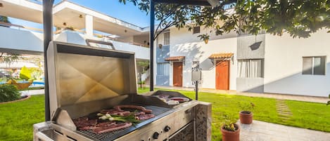 Un patio con una parrilla, plantas en macetas y un camino empedrado.